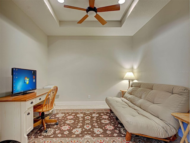 office space with a ceiling fan, baseboards, and a tray ceiling