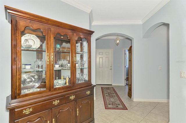 entrance foyer featuring crown molding, arched walkways, baseboards, and light tile patterned flooring
