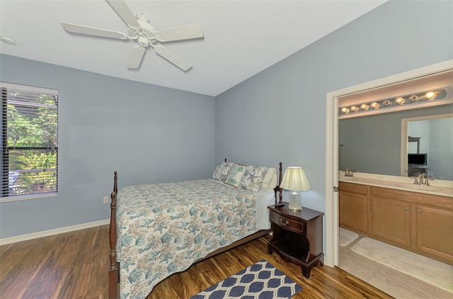 bedroom featuring ensuite bathroom, a sink, baseboards, and wood finished floors