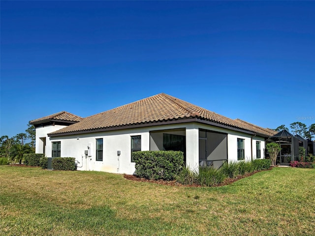 back of property featuring stucco siding, a tile roof, and a lawn