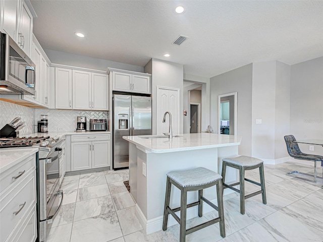 220 Sarezzo Cir, Nokomis, FL 34275 - kitchen with appliances with stainless steel finishes, a sink, light marble finish flooring, a breakfast bar area, and an island with sink