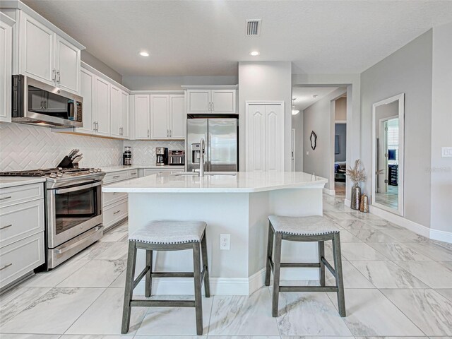 220 Sarezzo Cir, Nokomis, FL 34275 - kitchen with stainless steel appliances, light marble finish flooring, a kitchen breakfast bar, decorative backsplash, and light countertops