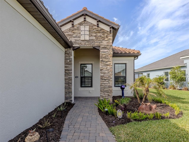 view of exterior entry featuring stucco siding, a lawn, a tile roof, and stone siding
