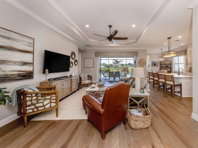living room featuring a wealth of natural light, a raised ceiling, ceiling fan, and light wood-style floors