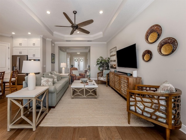 living room with recessed lighting, ceiling fan, a tray ceiling, ornamental molding, and wood finished floors