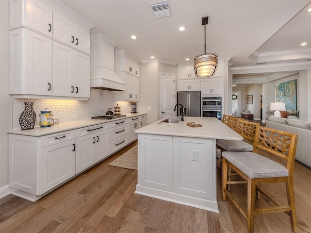 kitchen with light wood finished floors, a sink, decorative backsplash, stainless steel appliances, and visible vents