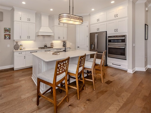 kitchen featuring stainless steel appliances, custom range hood, light countertops, baseboards, and crown molding
