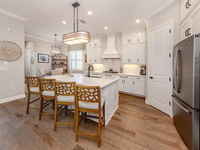 kitchen with light wood-style flooring, visible vents, premium range hood, freestanding refrigerator, and ornamental molding