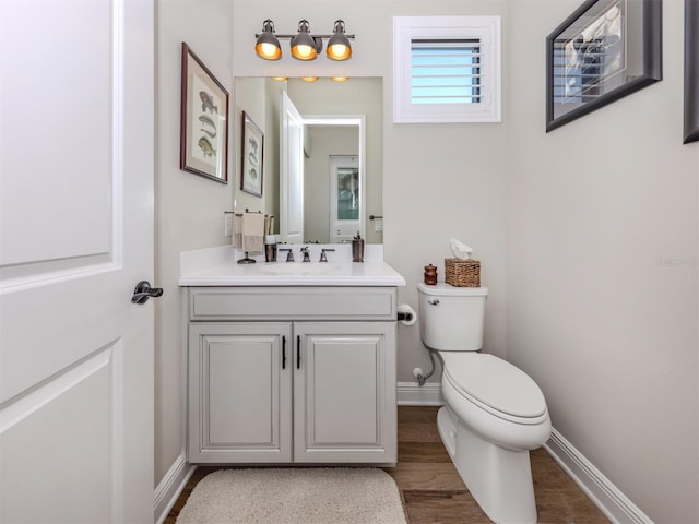 half bathroom featuring wood finished floors, vanity, toilet, and baseboards