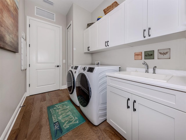 clothes washing area with a sink, visible vents, separate washer and dryer, cabinet space, and dark wood-type flooring