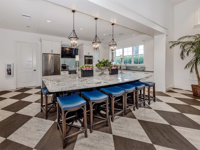 kitchen with light stone countertops, a breakfast bar, a large island with sink, high quality fridge, and white cabinetry