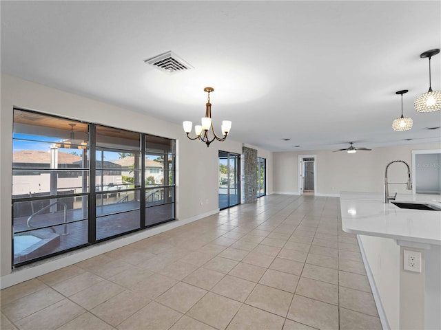 unfurnished dining area featuring a sink, light tile patterned floors, visible vents, baseboards, and ceiling fan with notable chandelier