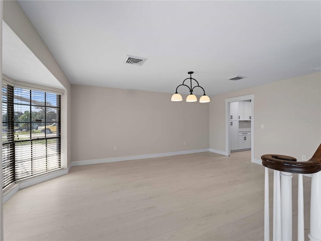 spare room featuring visible vents, light wood-type flooring, a notable chandelier, and baseboards
