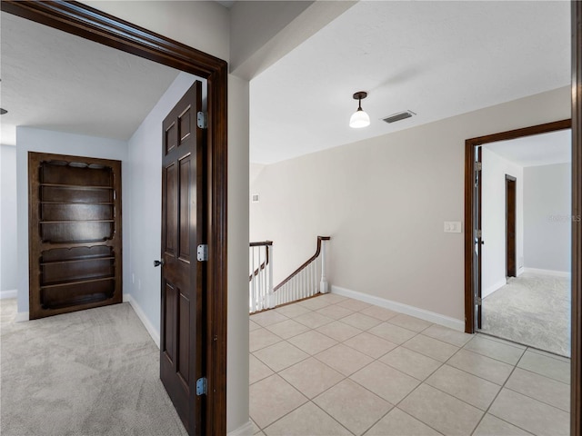 hallway featuring baseboards, visible vents, light carpet, and an upstairs landing