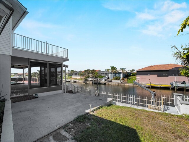 view of yard featuring fence, a water view, a balcony, and a sunroom