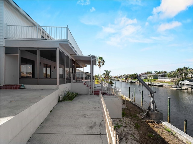 view of home's exterior featuring a sunroom, a water view, a boat dock, and a balcony