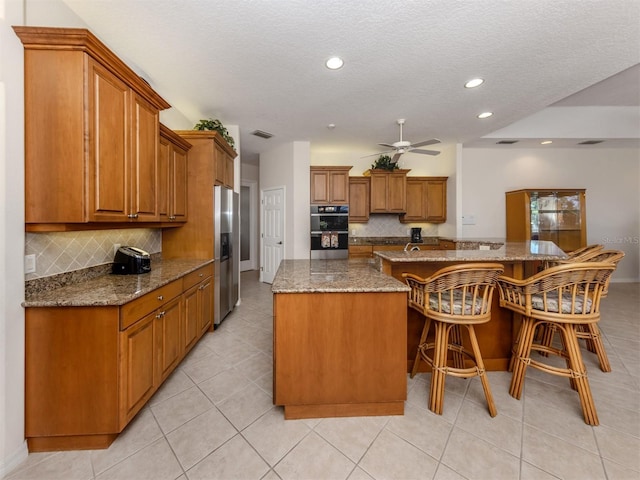 2022 Calusa Lakes Blvd, Nokomis, FL 34275 - kitchen with brown cabinets, a large island, stainless steel fridge, tasteful backsplash, and double oven