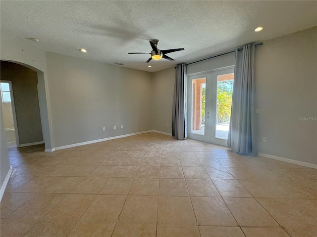 spare room with a textured ceiling, ceiling fan, light tile patterned floors, and arched walkways