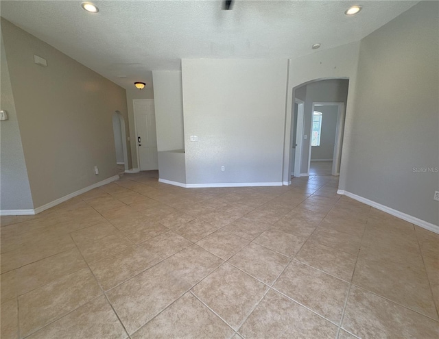 spare room with recessed lighting, light tile patterned flooring, a textured ceiling, baseboards, and arched walkways
