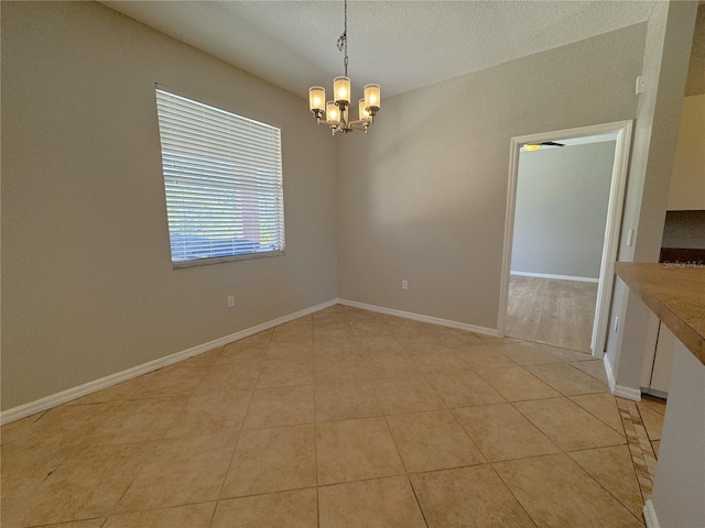 spare room featuring light tile patterned floors, a notable chandelier, and baseboards