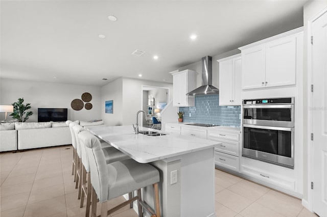 kitchen with a sink, black electric stovetop, wall chimney exhaust hood, double oven, and open floor plan