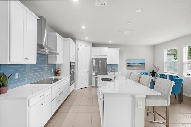 kitchen with a sink, stainless steel appliances, decorative backsplash, visible vents, and wall chimney range hood