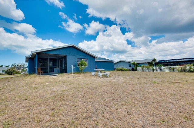 back of property featuring a sunroom, stucco siding, fence, and a yard
