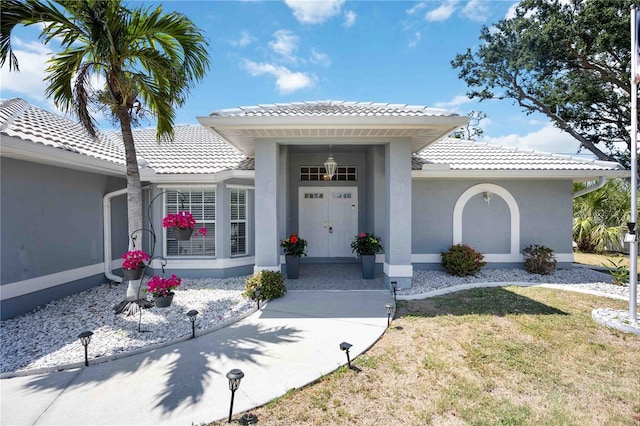 doorway to property with stucco siding, a tile roof, and a lawn