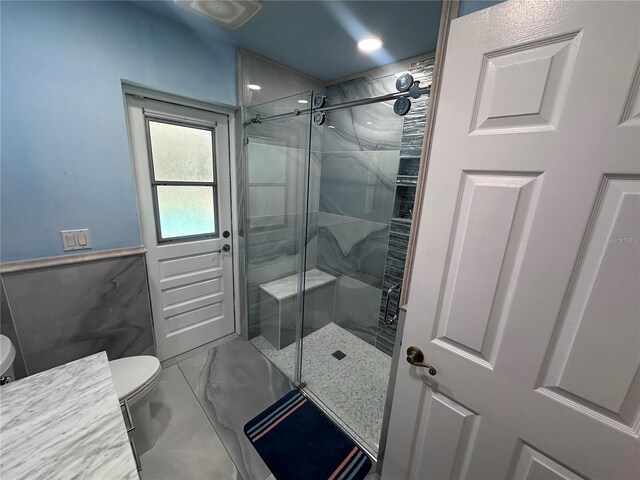 bathroom featuring a wainscoted wall, a shower stall, toilet, and marble finish floor