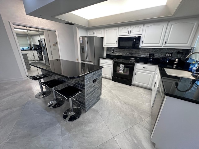 kitchen featuring white cabinets, a breakfast bar, dark countertops, black appliances, and backsplash