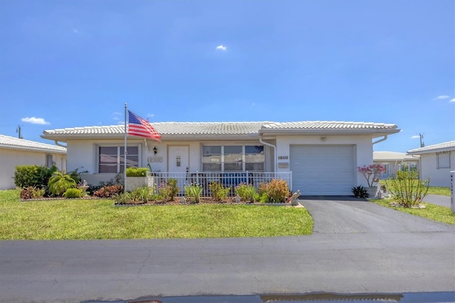 ranch-style home featuring a tiled roof, driveway, a front yard, an attached garage, and stucco siding