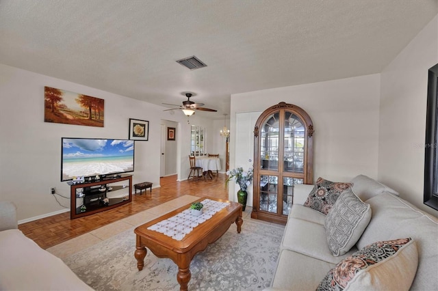 living area with a ceiling fan, a textured ceiling, visible vents, and baseboards