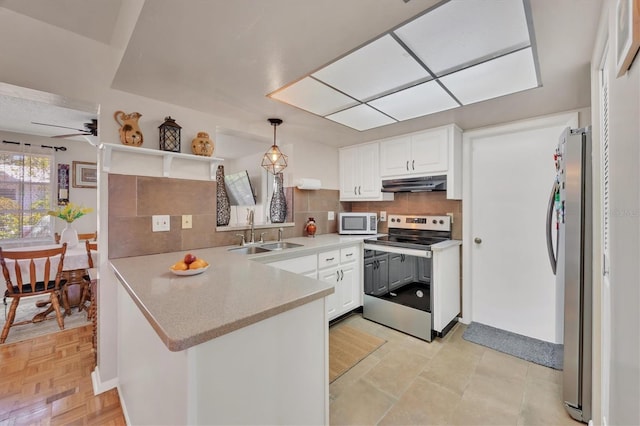 kitchen with appliances with stainless steel finishes, a sink, a peninsula, tasteful backsplash, and under cabinet range hood