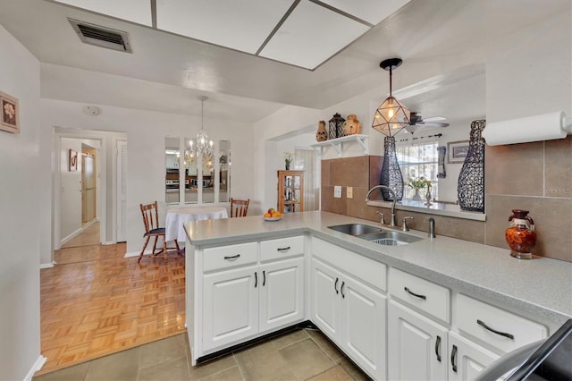 kitchen featuring visible vents, a peninsula, light countertops, white cabinets, and a sink