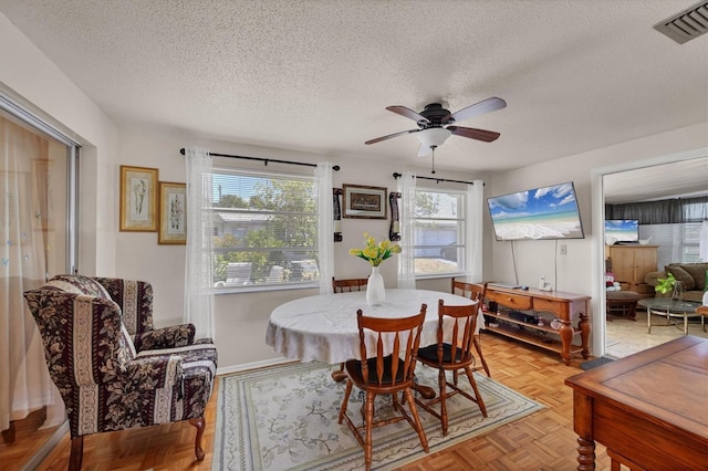 dining space with a healthy amount of sunlight, a ceiling fan, a textured ceiling, and visible vents