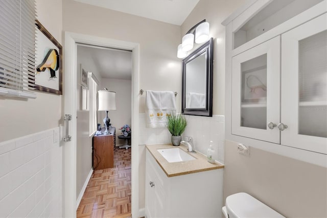 bathroom with wainscoting, tile walls, vanity, and toilet