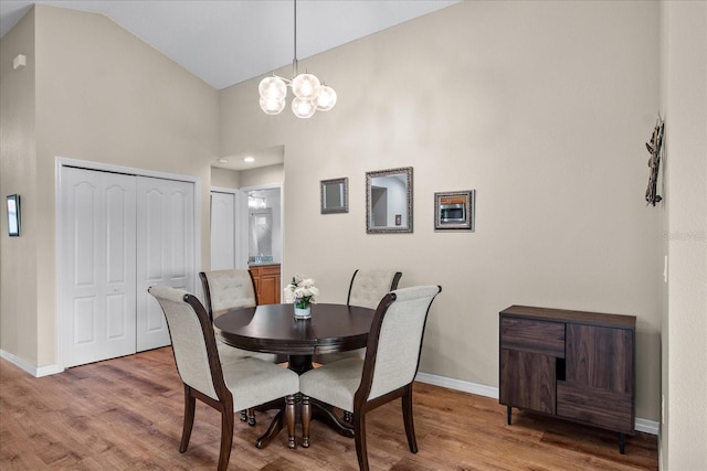 dining area with baseboards, a notable chandelier, wood finished floors, and high vaulted ceiling