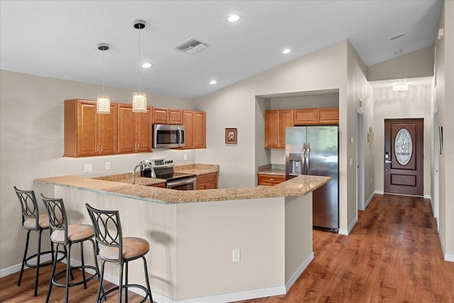 kitchen featuring brown cabinets, appliances with stainless steel finishes, a peninsula, lofted ceiling, and visible vents