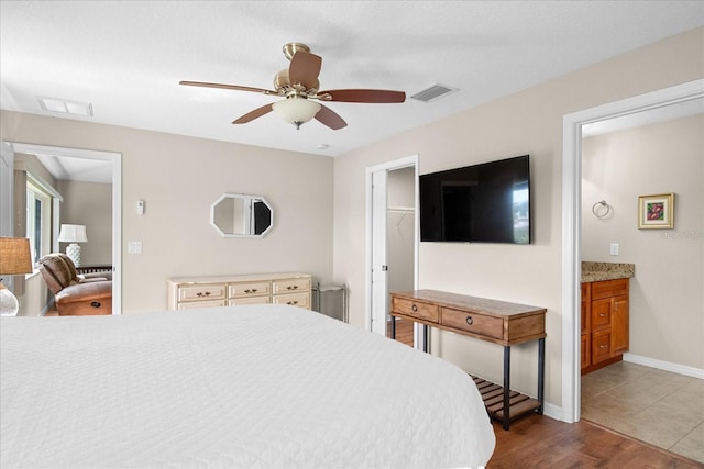 bedroom with visible vents, ensuite bath, a walk in closet, and wood finished floors