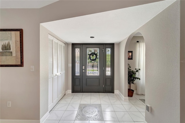 entrance foyer with light tile patterned flooring, arched walkways, and baseboards