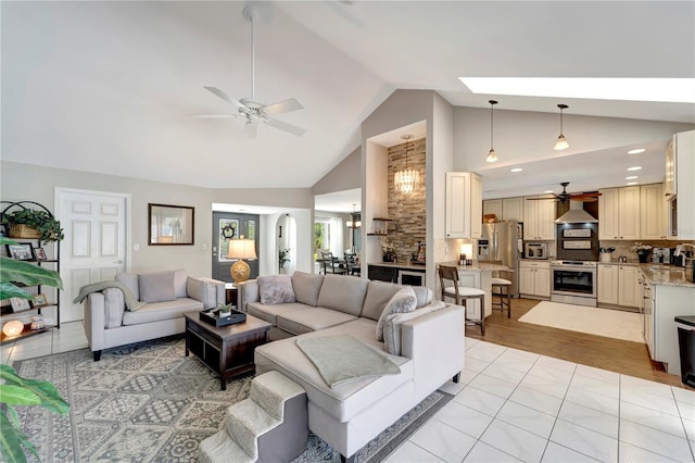 living area with high vaulted ceiling, a skylight, ceiling fan, and light wood-style flooring