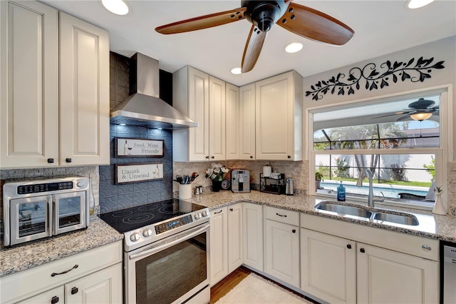 kitchen featuring a ceiling fan, wall chimney exhaust hood, appliances with stainless steel finishes, and a sink