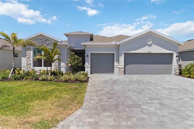 prairie-style house with an attached garage, stone siding, stucco siding, a front yard, and decorative driveway