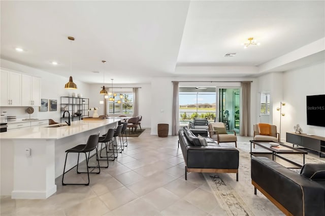 living room with visible vents, light tile patterned floors, baseboards, a tray ceiling, and recessed lighting