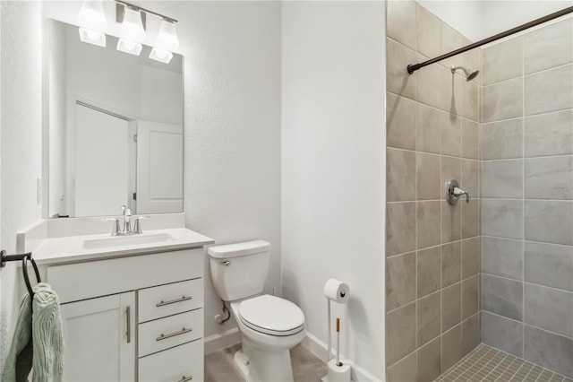 bathroom with toilet, baseboards, a tile shower, and vanity