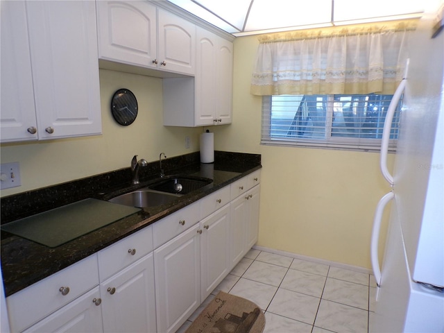 kitchen with a sink, white cabinetry, dark stone countertops, and freestanding refrigerator
