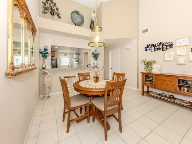 dining area with light tile patterned floors, visible vents, baseboards, and a high ceiling