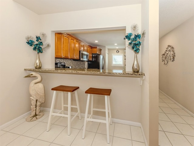 kitchen featuring light stone countertops, brown cabinetry, baseboards, backsplash, and stainless steel appliances