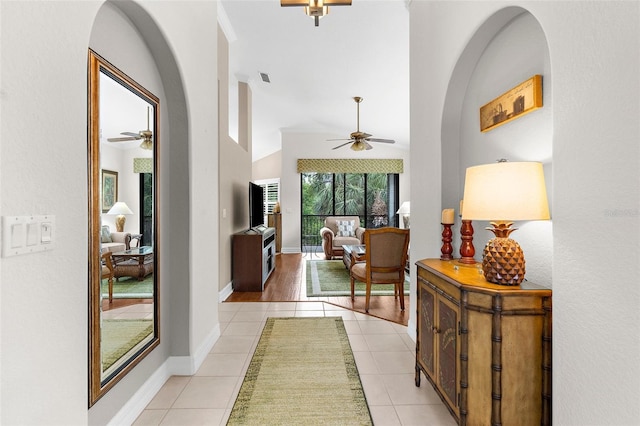 hallway featuring visible vents, lofted ceiling, light tile patterned flooring, baseboards, and arched walkways