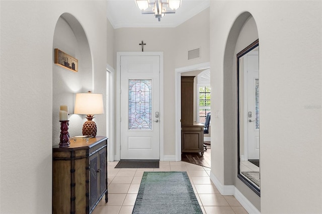 entryway with crown molding, a notable chandelier, baseboards, light tile patterned floors, and visible vents